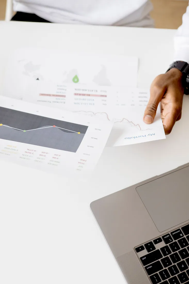 Person prüft Diagramme auf einem Laptop und ausgedruckten Unterlagen