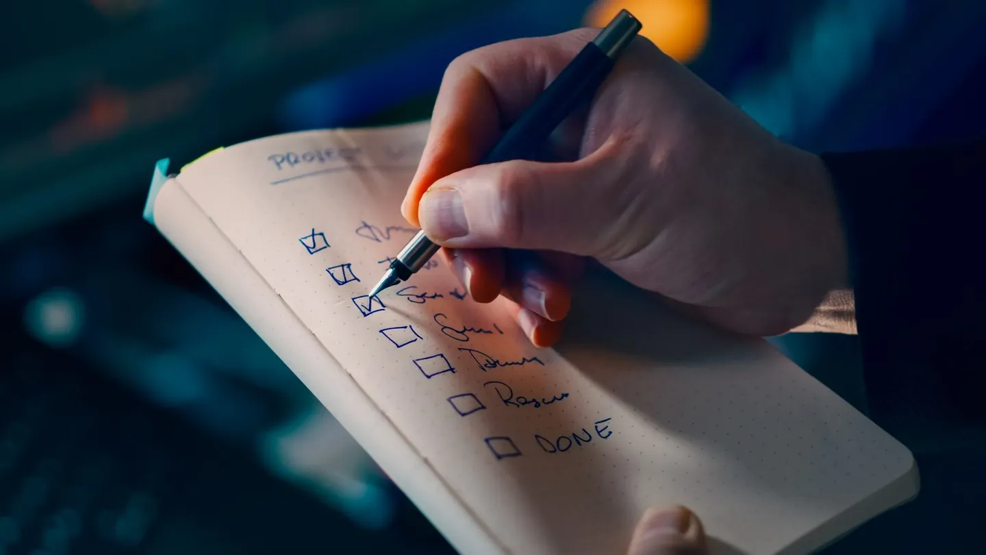 Hand schreibt eine Checkliste in ein Notizbuch