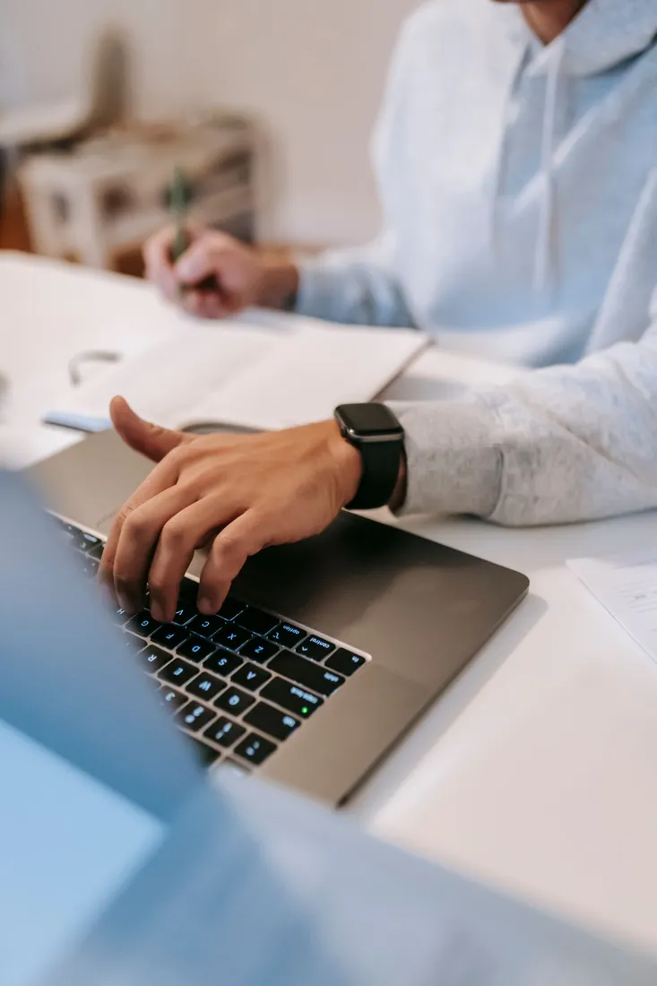 Person arbeitet mit einem Laptop und Notizbuch am Tisch