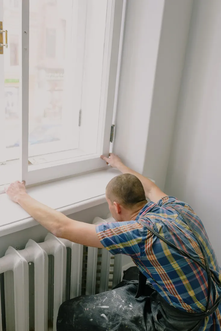 Person montiert ein Fenster oberhalb eines Heizkörpers