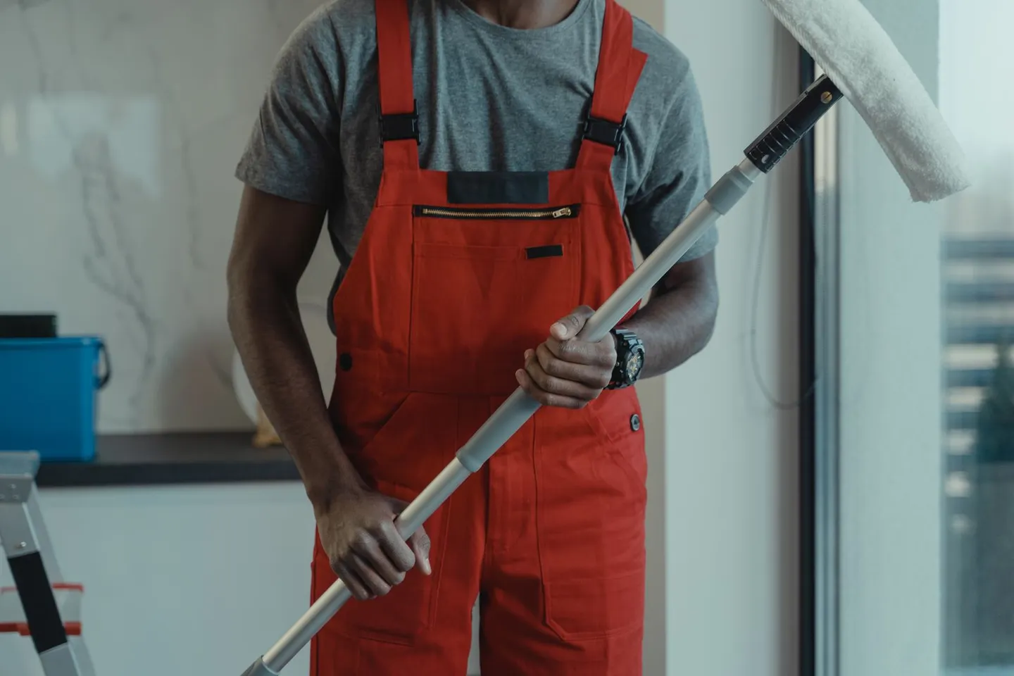 Person in roter Arbeitskleidung mit einem Wischmopp