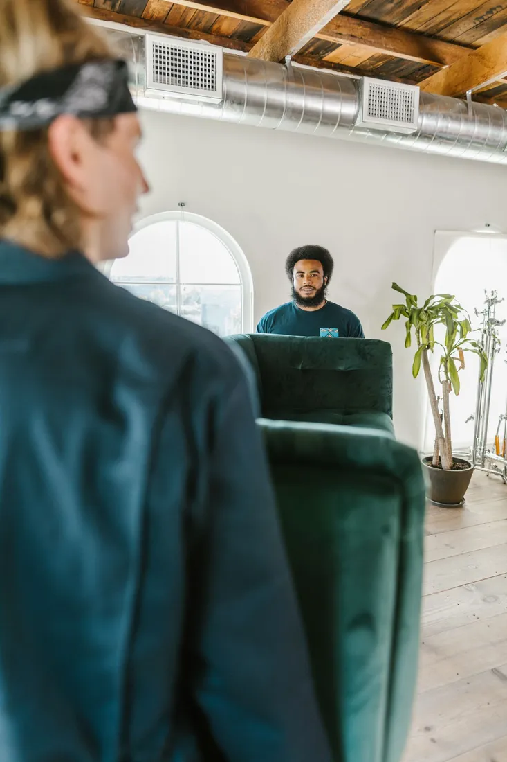 Zwei Männer tragen ein grünes Sofa durch eine Wohnung