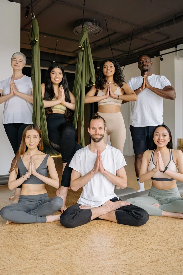 Gruppe mit vor der Brust zusammengelegten Händen im Yogastudio